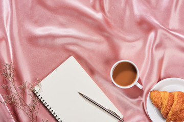 Minimal styled flat lay table with open notebook, croissant and tea.