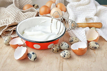 The beater eggs and a bowl with beaten egg whites on a wooden table.