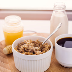 healthy breakfast fresh cereal, milk bottle, coffee cup and honey jar, toned warm sunny morning light
