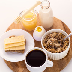healthy breakfast fresh cereal, cheese sandwich, hard boiled egg, milk bottle, coffee cup and honey jar, toned warm sunny morning light