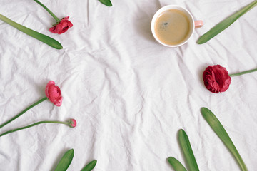 Cup of coffee and pink anemone flowers on cotton sheet. Flat lay, top view, copy space, frame