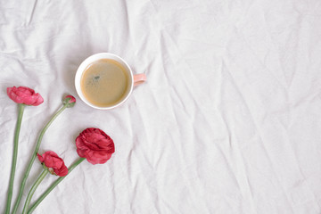 Cup of coffee and pink anemone flowers on cotton sheet. Flat lay, top view, copy space