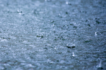 Rain drops rippling in a puddle with blue sky reflection