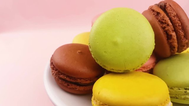Sweet color macaroons or macaron rotated on white plate on pastel pink surface. Close up.