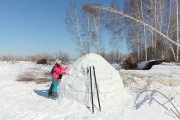 Happy woman skier in a red jacket standing near an igloo   on a snowy glade, Siberia, Russia