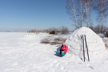 Happy woman skier in a red jacket sitting near an igloo   on a snowy glade, Siberia, Russia