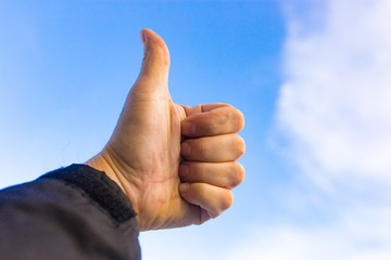 Male hand against a blue sky with clouds