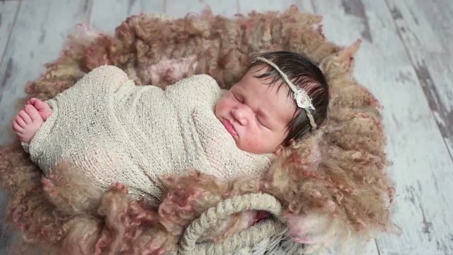 Tightly swaddled adorable baby-girl sleeping in a fancy baby backet covered with fur