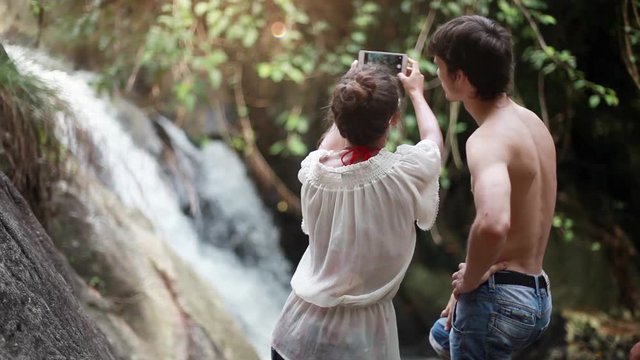 Travel couple fun taking photo by waterfall using smartphone. People visiting famous tourist attractions and landmarks on Koh Samui. 1920x1080