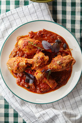 Chicken legs cooked in italian cacciatore style with tomato sauce and fresh basil on green checkered table-cloth