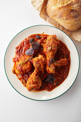 Chicken legs cooked in italian cacciatore style with tomato sauce and fresh basil on white table