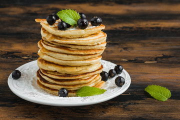 Stack of sweet pancakes with fresh berries and mint on white plate on wooden rustic table