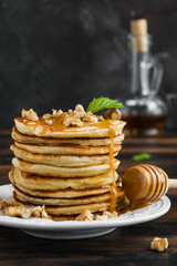 Stack of pancakes with honey and walnuts on white plate on wooden rustic table, copy space