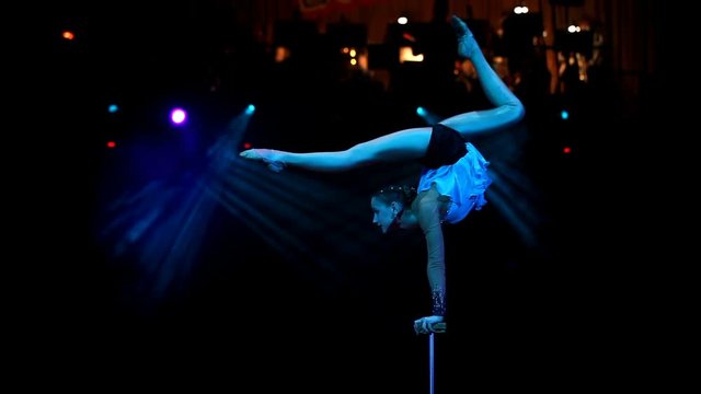 Young flexible acrobat girl doing equilibre balance on a cube in circus