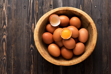 Yellow chicken eggs in a wooden bowl on a table, top view