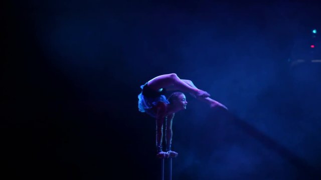 Young flexible acrobat girl executes tricks on a cube in circus