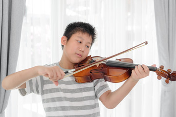 Happy Asian boy playing violin near window at home.