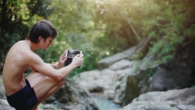 Young man traveler taking photo with beautiful waterfall on sunny day. 1920x1080