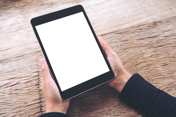 Mockup image of hands holding black tablet pc with blank white screen on vintage wooden table
