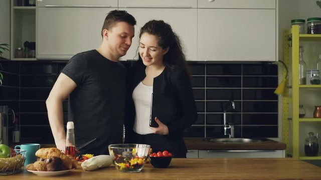 young beautiful businesswoman came home from work ah home, her handsome husband is cooking in the kithcen, she is asking about dinner, they are kissing and laughing