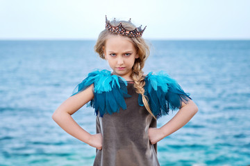 stern little princess girl in the crown watch frowningly, stands akimbo © Tatsiana