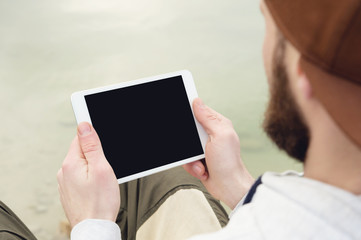 Close-up of a horde in a brown cap in the open air holds a white tablet pc in his hands. A bearded man looks at the tablet. OTS view from behind the shoulder