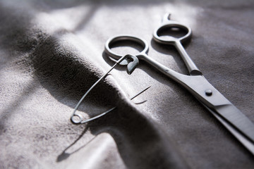 Scissors and a pin on a gray fabric with a rough surface