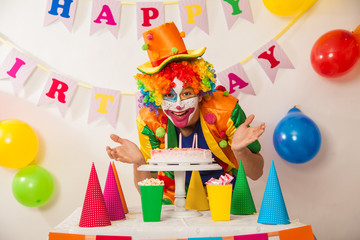 Fototapeta na wymiar Clowns are a boy in bright costumes at the child's birthday. A table with refreshments and a cake. The explosion of emotions and the fun of the circus. greed and desire to eat cake
