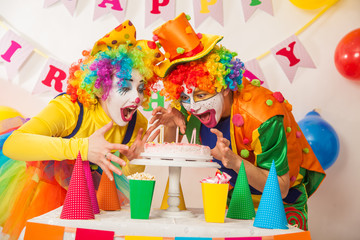 Clowns are a boy and a girl in bright costumes at the child's birthday. A table with refreshments and a cake. The explosion of emotions and the fun of the circus. greed and desire to eat cake