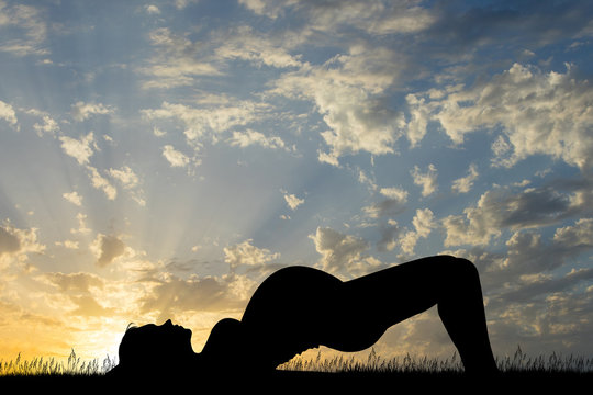 a pregnant girl doing yog at sunset