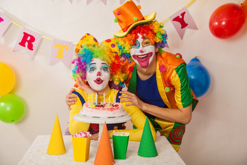 Clowns are a boy and a girl in bright costumes at the child's birthday. A table with refreshments and a cake. The explosion of emotions and the fun of the circus. greed and desire to eat cake