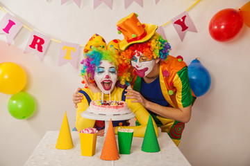 Clowns are a boy and a girl in bright costumes at the child's birthday. A table with refreshments and a cake. The explosion of emotions and the fun of the circus. greed and desire to eat cake
