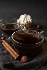 Close-up. Transparent cup of coffee, cinnamon sticks on a grey linen napkin. Dark background