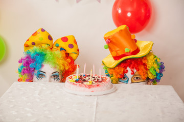 Clowns are a boy and a girl in bright costumes at the child's birthday. A table with refreshments and a cake. The explosion of emotions and the fun of the circus. greed and desire to eat cake