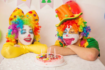 Clowns are a boy and a girl in bright costumes at the child's birthday. A table with refreshments and a cake. The explosion of emotions and the fun of the circus. greed and desire to eat cake