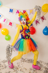 A clown girl in a bright suit at the baby's birthday party. The explosion of emotions and the fun of the circus. Paper disco made of silver paper