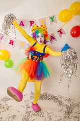 A clown girl in a bright suit at the baby's birthday party. The explosion of emotions and the fun of the circus. Paper disco made of silver paper