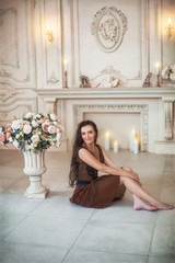 Obraz na płótnie Canvas Lovely girl in brown dress sitting on floor near blooming flowers in luxurious room