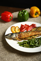 Healthy and proper food, grilled fish and vegetables with lemon and green beans on a white plate. On the background of pepper, burlap and wooden table. Low-calorie food