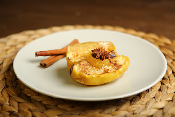 On the plate is a baked apple, near cinnamon, anise. Wicker substrate and wooden table, composition. Close-up