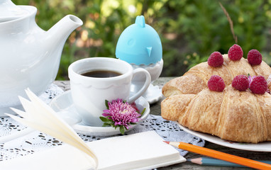 Breakfast with cup of coffee and croissants with raspberry. Egg on white a lace tablecloth with green grass background. 