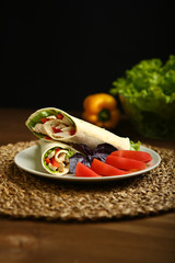 Shaurma without sauce with chicken, pepper, lettuce. Low-calorie roll from pita bread, next to purple basil and slices of tomatoes. Without roasting, raw. In the background pepper and lettuce leaves