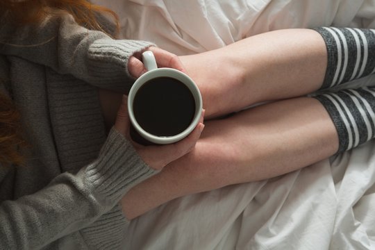 Woman holding mug of black coffee in bedroom