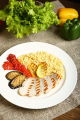 Grilled chicken with slices, with vegetables, bulgur on a white plate. In the background, lettuce leaves, color pepper. Low-calorie, dietary food for a healthy lifestyle.