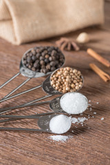 Food ingredient for cooking on a wooden board. Measuring spoons with salt, sugar, coriander seed and black pepper.