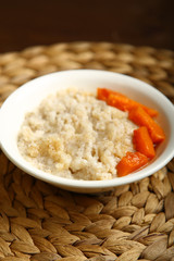 Low-calorie porridge for a healthy diet and lifestyle. Barley with honey and bits of orange pumpkin in a deep white plate. Dark background, wooden table and wicker stand