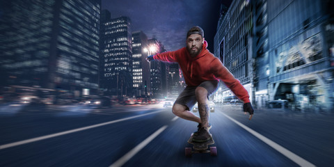 Hipster man rides on a longboard in the streets at night