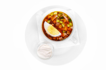 Okroshka with egg and sour cream. On a napkin in a white plate isolated white. Serving dishes in a cafe, restaurant, for a menu. View from above