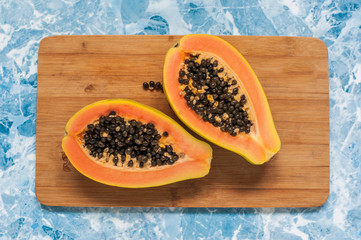 The cut papaya lies on a wooden background. The two halves of the exotic fruit