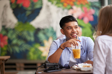 Cheerful Asian man chatting with his Caucasian girlfriend at cafe
